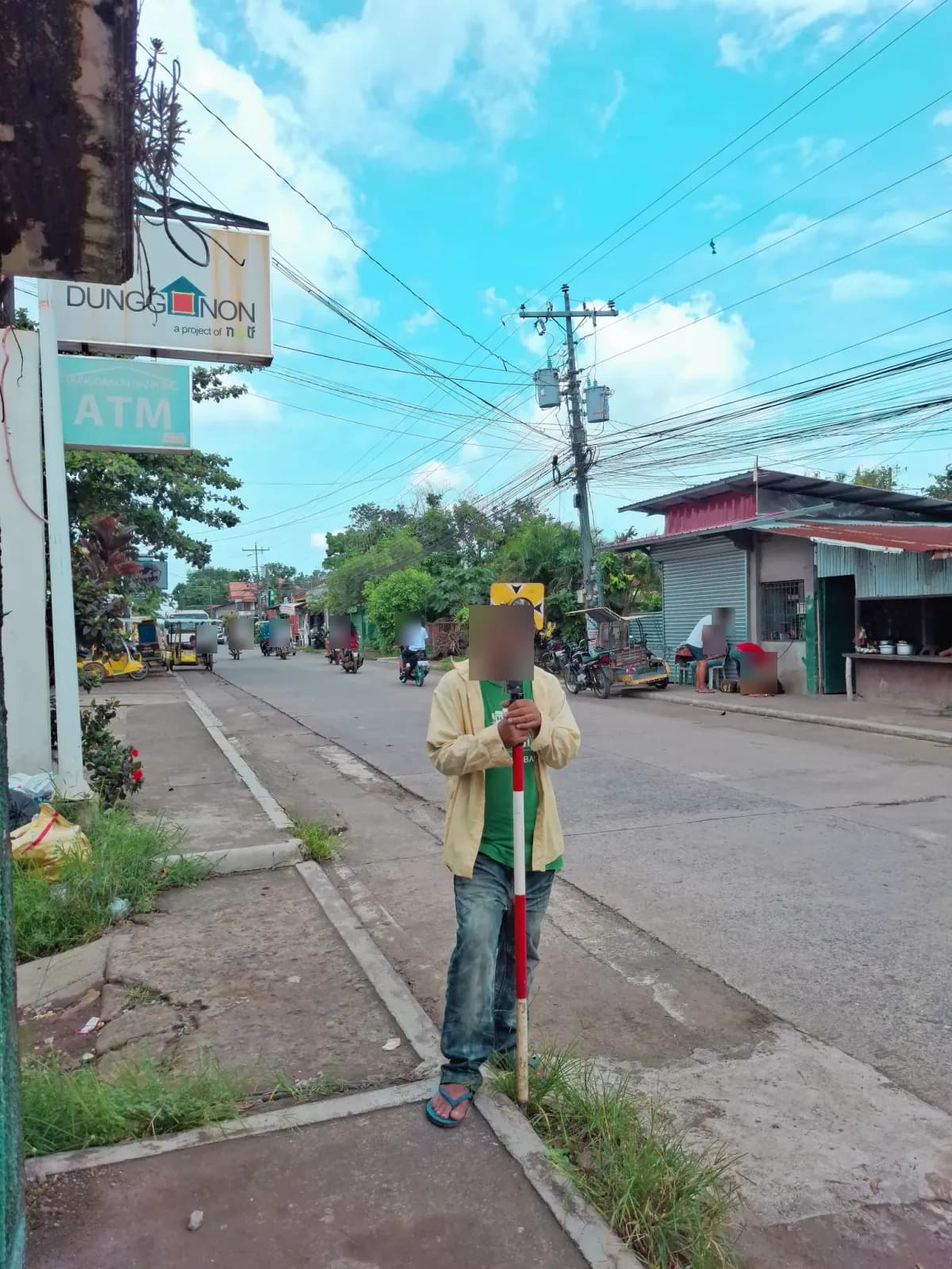 Crew member holding a prism pole upright at a curbside observation point on a neighborhood street