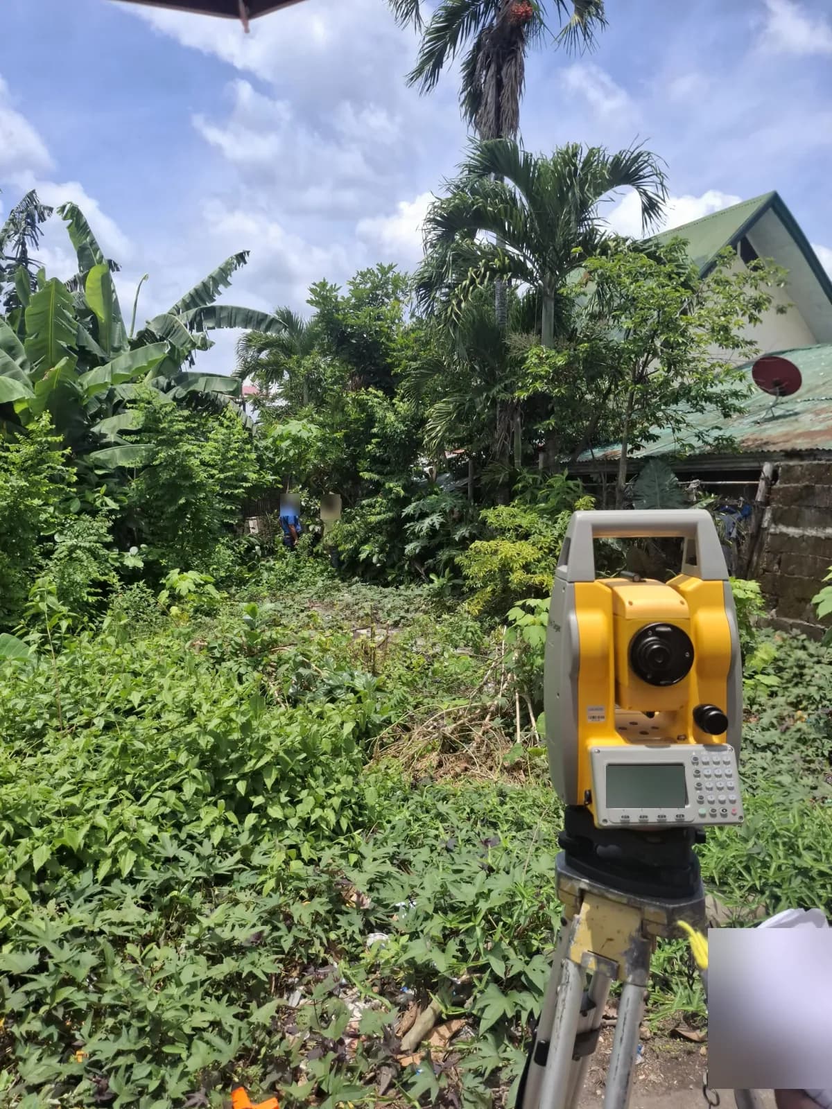 Total station and field notebook in the foreground with crew members inside a vegetated lot