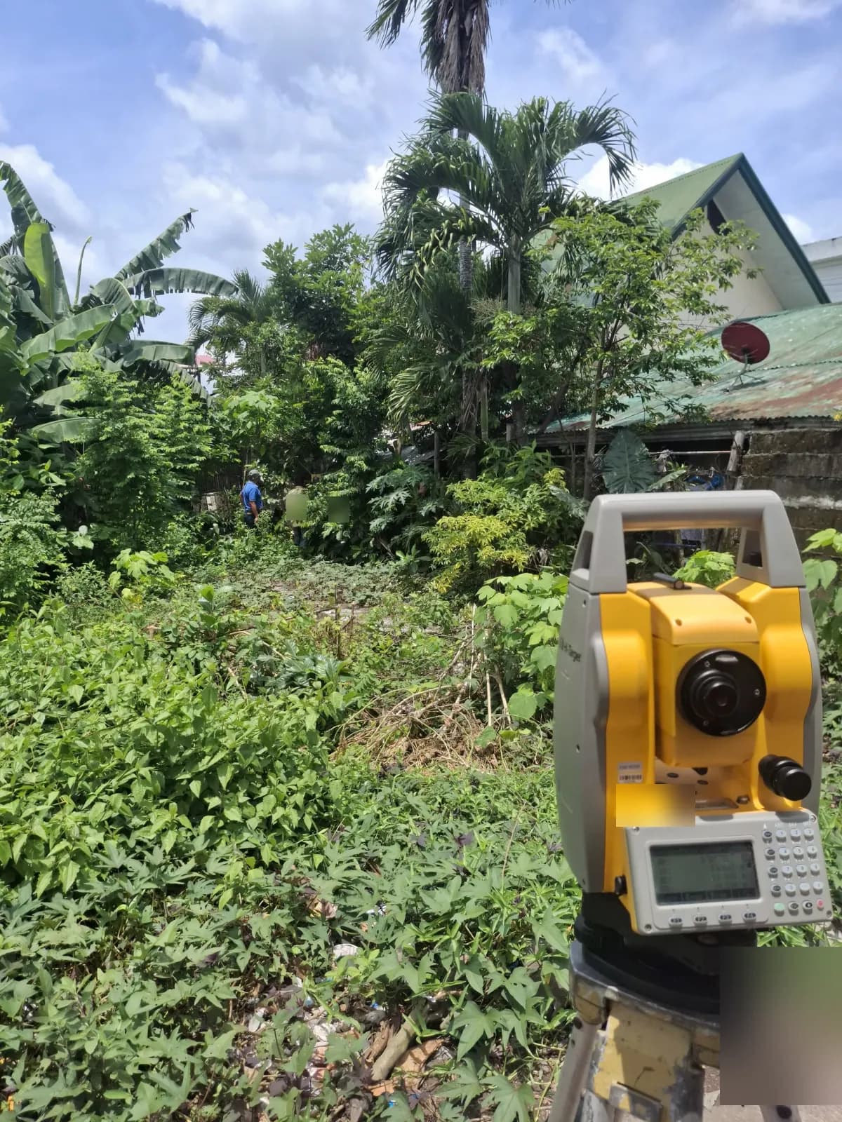 Tripod-mounted total station beside a field notebook with an observation point beyond the vegetation