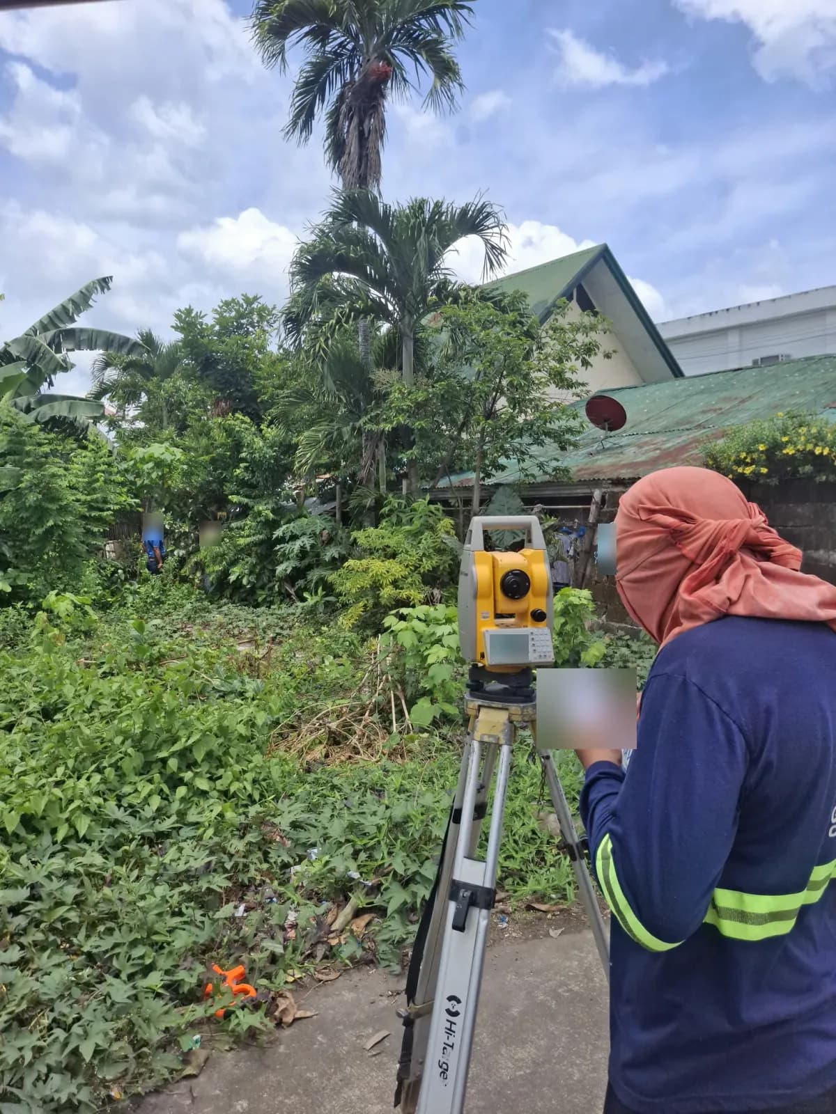 Survey operator using a field notebook beside a total station facing the overgrown lot