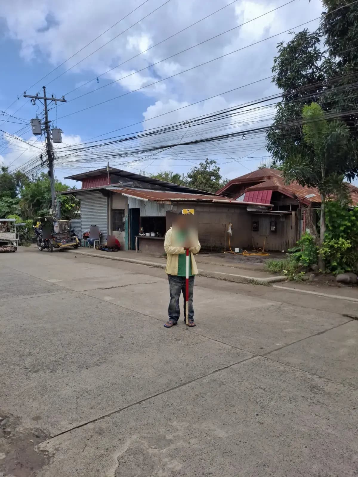 Field crew member holding a survey prism upright on a concrete road near neighboring buildings