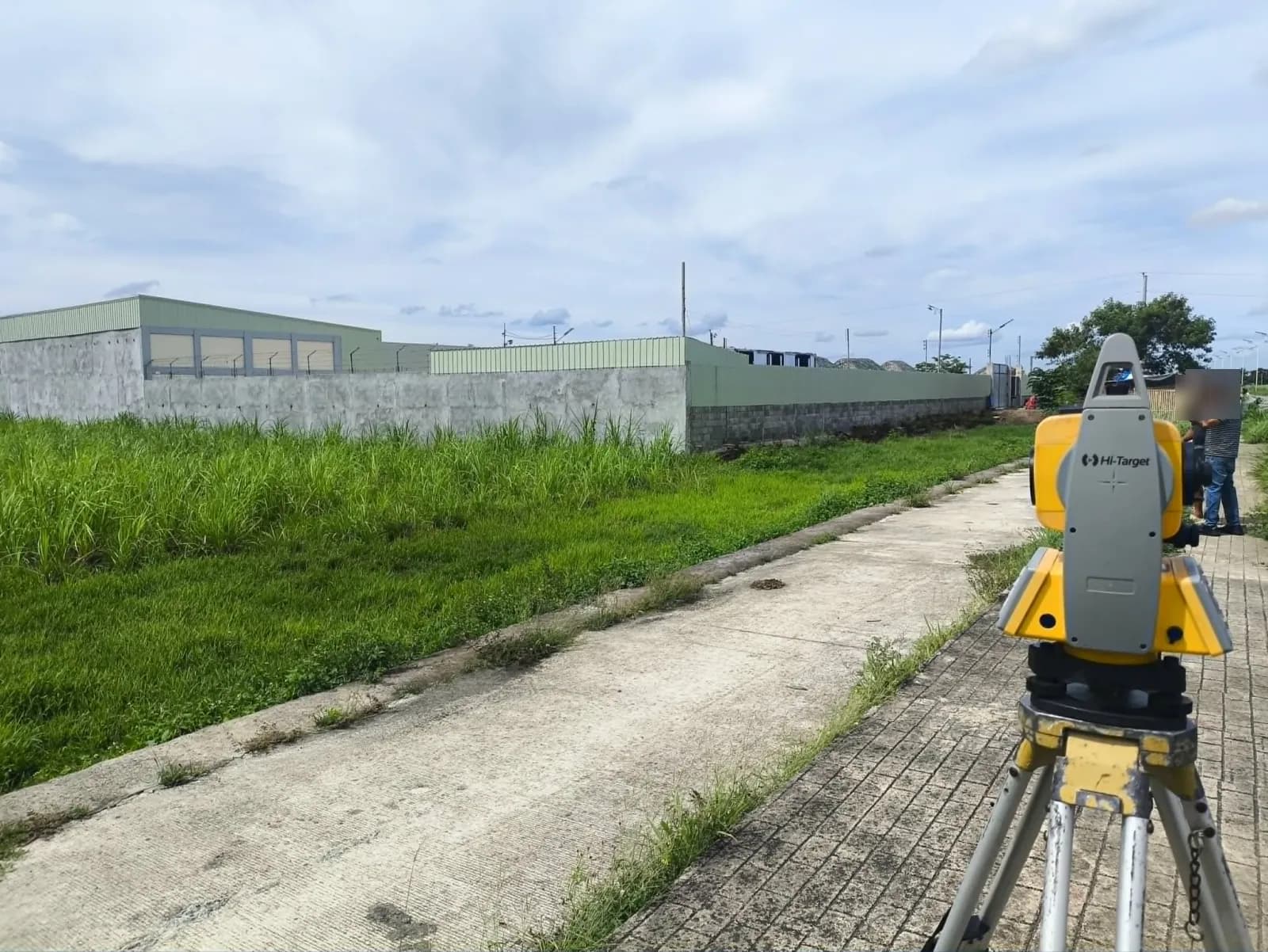 Rear view of a total station beside a grassy lot and a long concrete wall around a green-roofed building