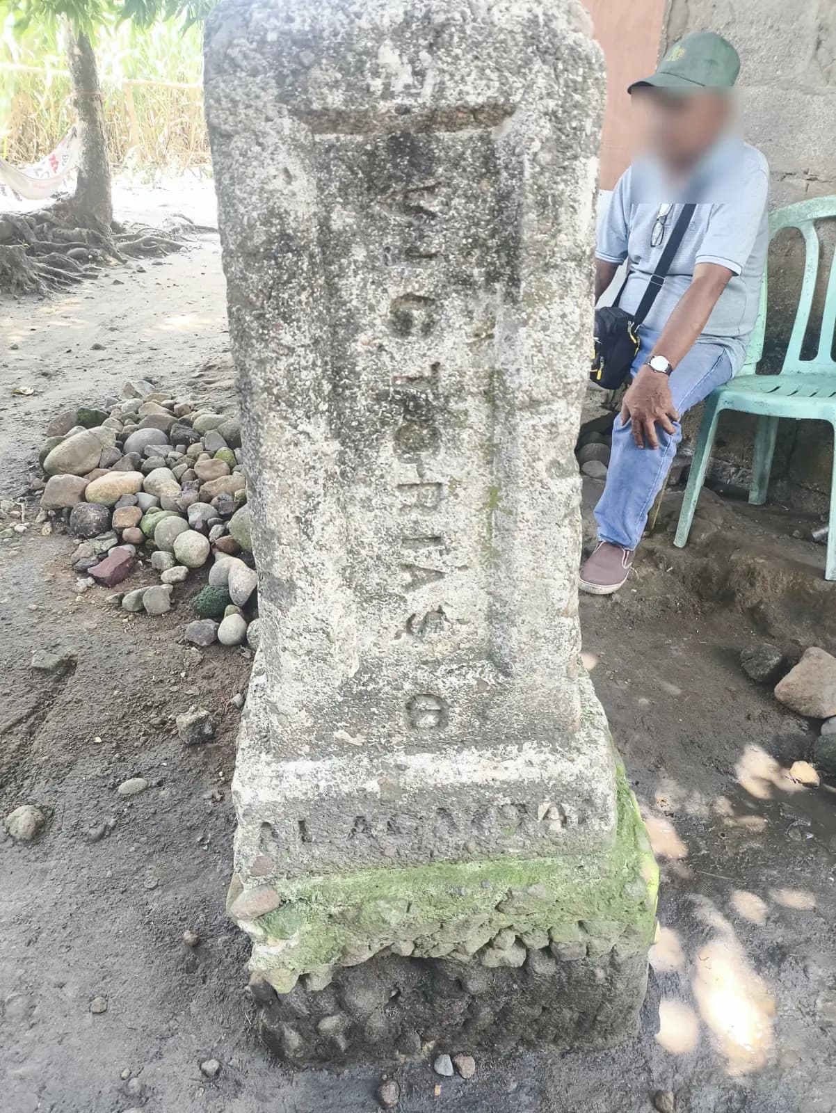 Concrete monument beside a seated person near a building at the E. B. Magalona survey site