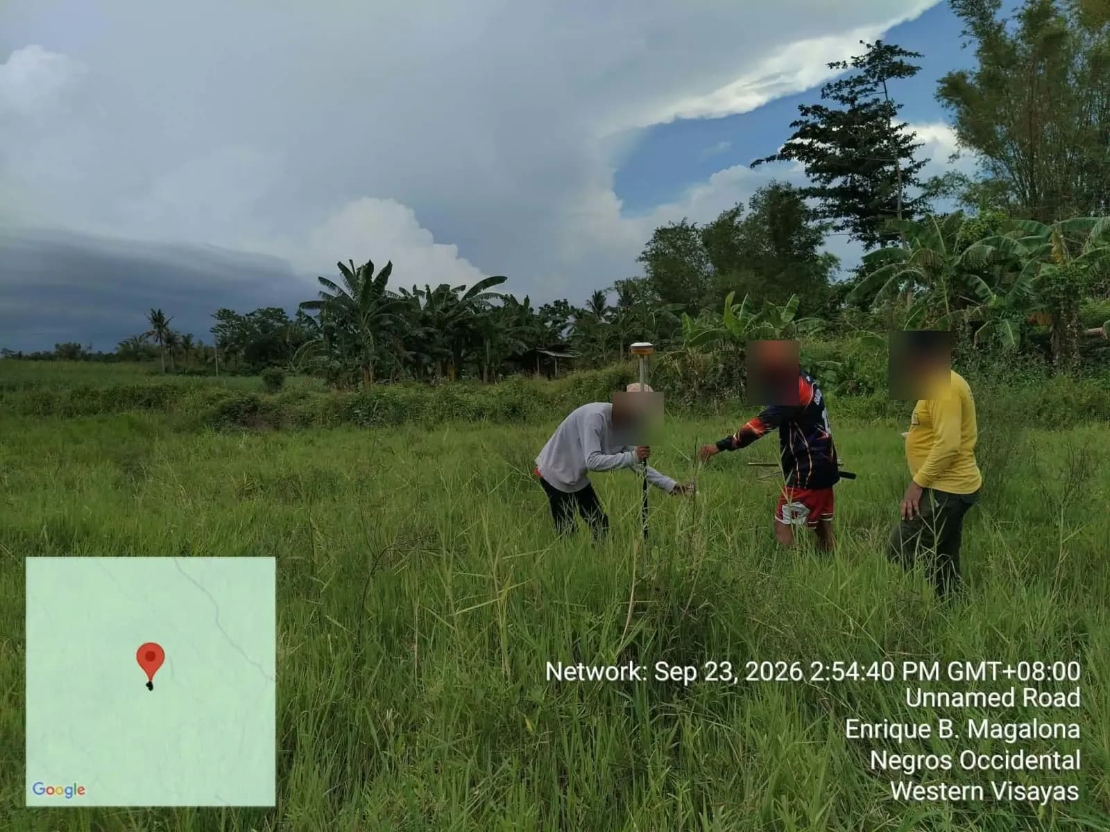 Three crew members checking the ground beside a GNSS pole in open grassland