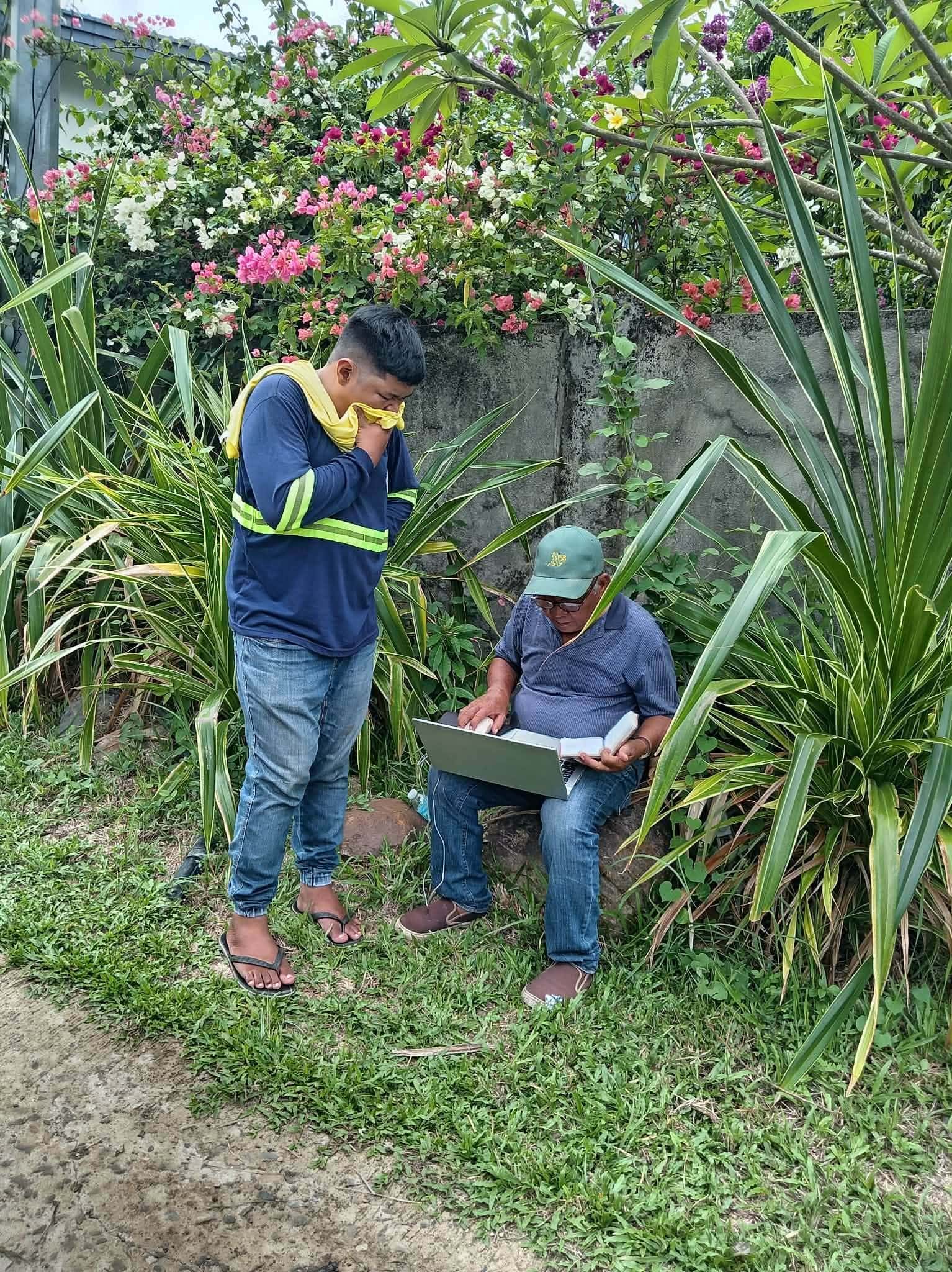 Two Leonor Surveying Services crew members reviewing land records on a laptop outdoors in Murcia, Negros Occidental