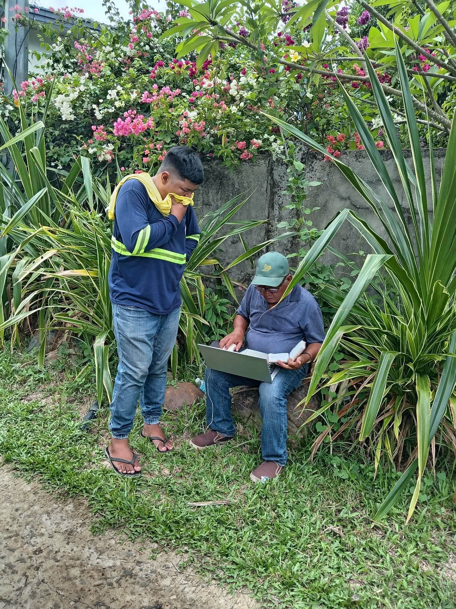 Two Leonor Surveying Services crew members reviewing survey records on a laptop outdoors in Murcia, Negros Occidental