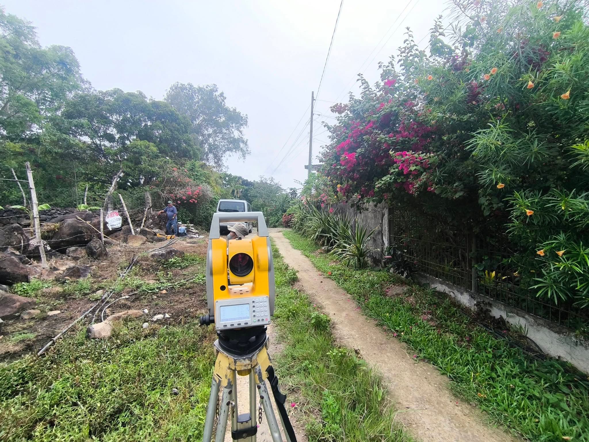 Leonor Surveying Services Hi-Target total station on a tripod aimed at rocky, boulder-strewn terrain with bamboo fence posts and banana trees during a relocation survey in Murcia, Negros Occidental