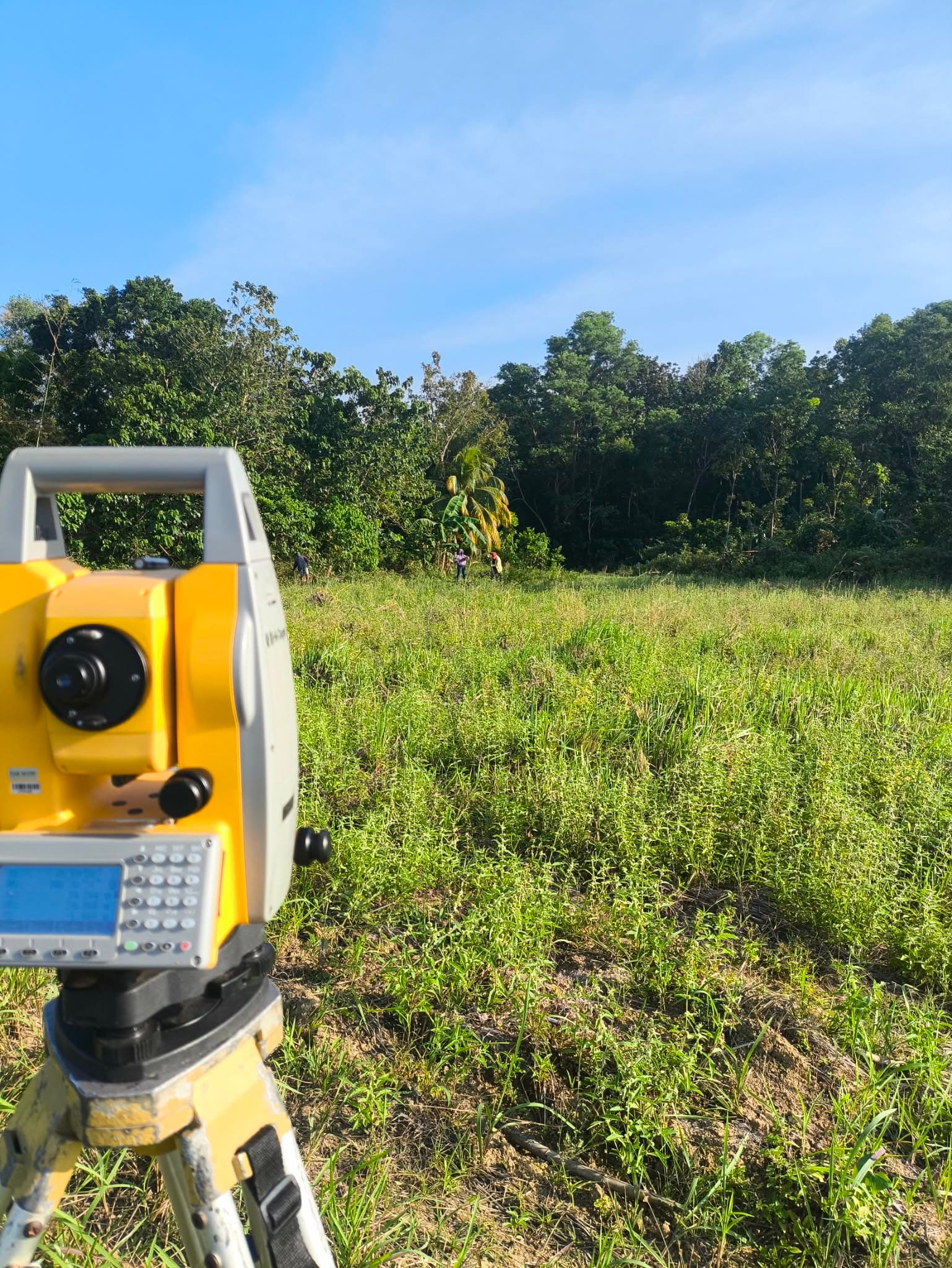 Yellow total station on a tripod as the Leonor survey team works in a green field in Negros